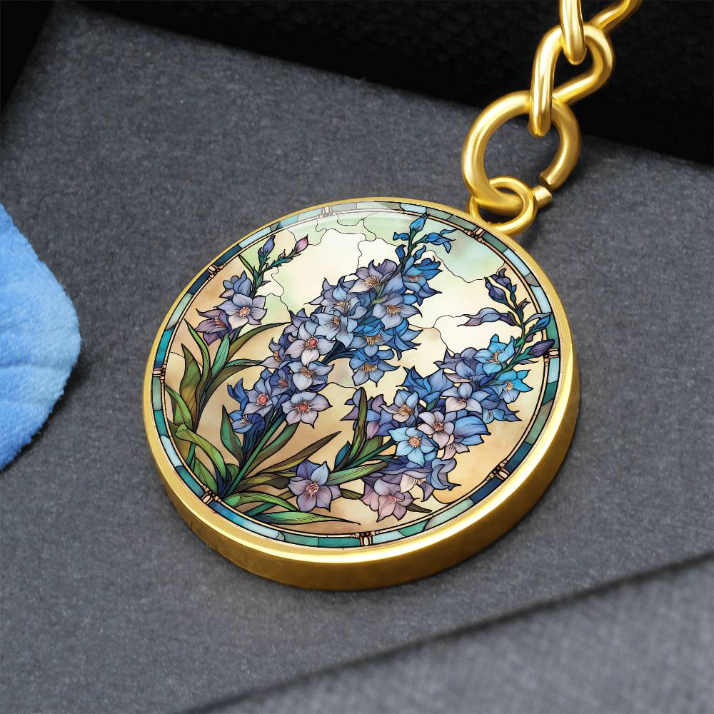 An elegant gold pendant Larkspur Flower Keychain. The colors are blue, purple, green and tan. This jewelry offers personalization with an engraving option for a name.