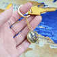 Woman holding An elegant gold pendant Larkspur Flower Keychain. The colors are blue, purple, green and tan. This jewelry offers personalization with an engraving option for a name.
